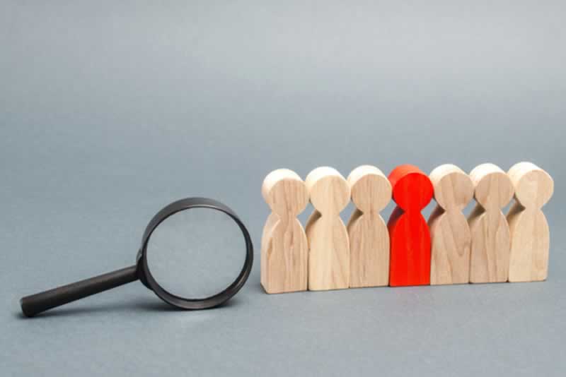 lupa y conjunto de figuras de madera de personas siendo una de ellas toja
