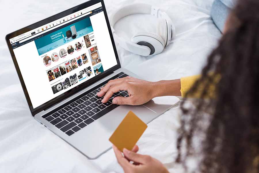 Mujer sostiene tarjeta de crédito dorada mientras realiza compras online en amazon