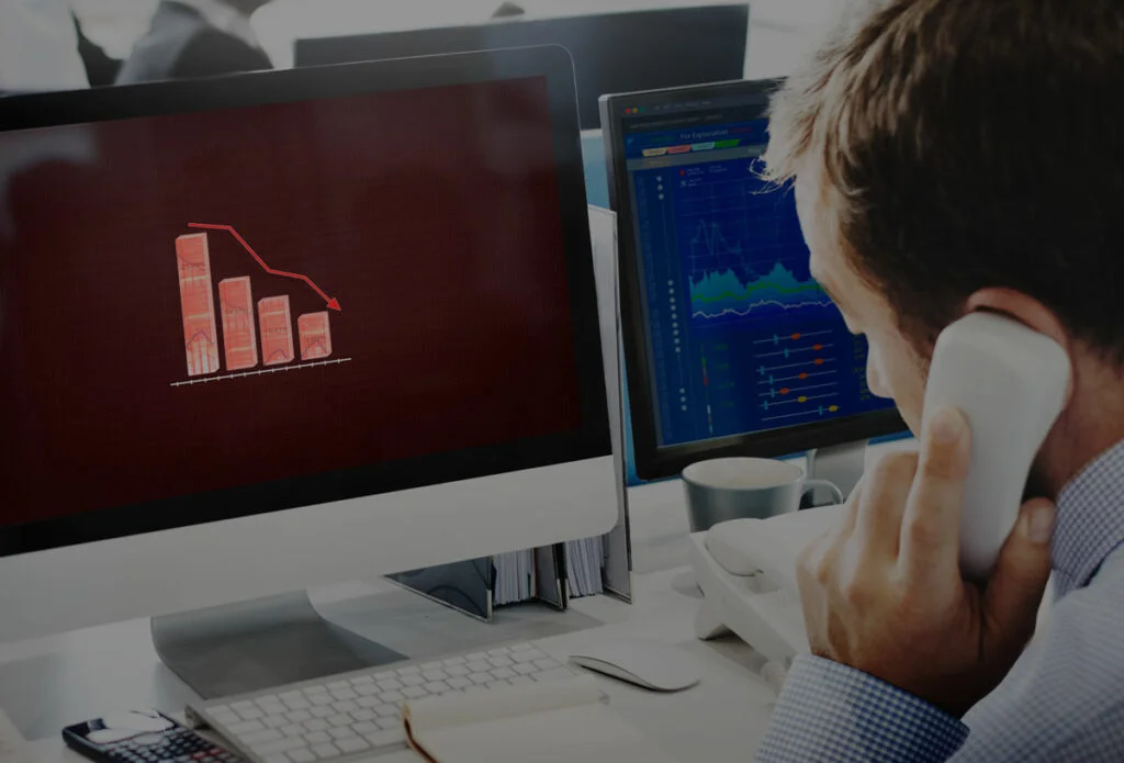 Hombre de negocios hablando por teléfono mientras observa un gráfico de caída en la pantalla de su computadora, representando crisis financiera o pérdida en inversiones