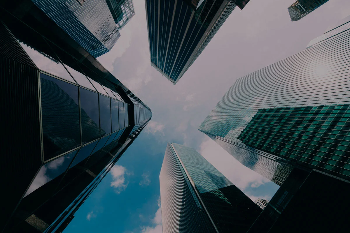 Vista desde abajo de modernos rascacielos de cristal reflejando el cielo, simbolizando el crecimiento empresarial y el mundo financiero